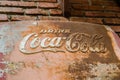 Classic trademark branding logo of CoCa-Cola on rusty metal sheet with red brick wall.